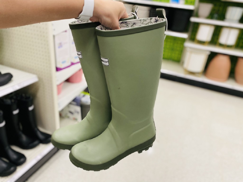 woman holding up a pair of rubber rain boots in a target store