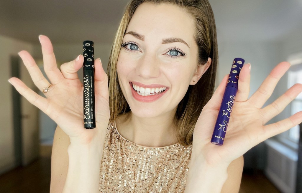 woman holding up two tubes of winky lux mascaras smiling