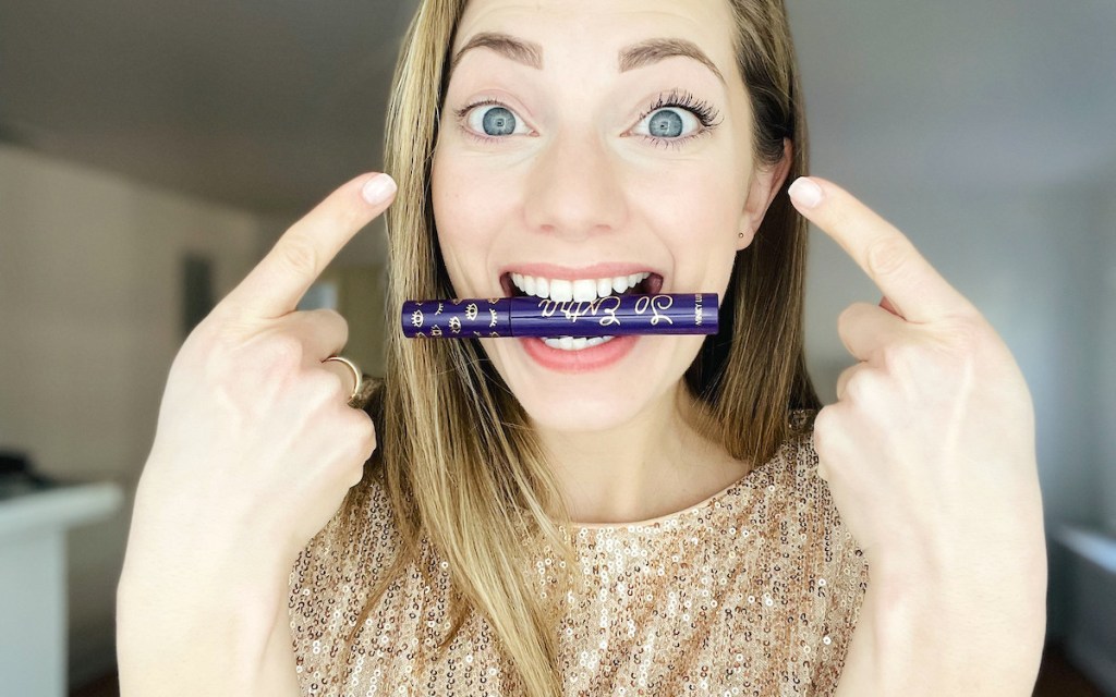 woman with winky lux mascara in mouth pointing to eyes