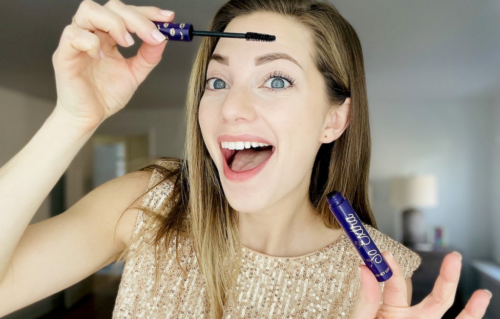 woman holding purple tube of mascara looking surprised