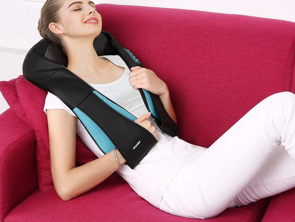 woman laying on a couch and using a neck massager