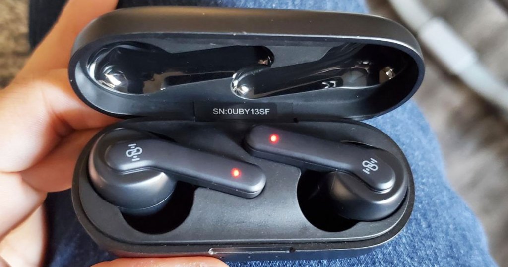 person holdng earbuds in black charging case