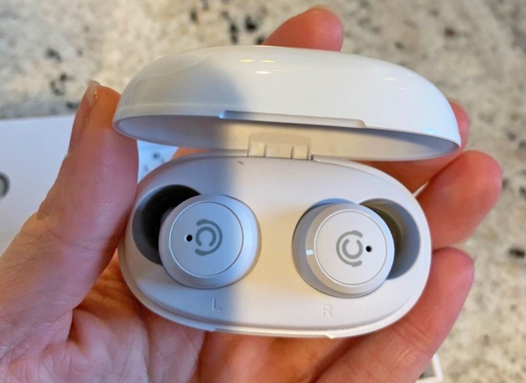 person holding pair of white earbuds in charging case