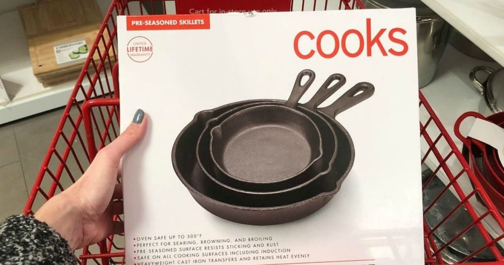 hand holding Cooks 3pc cast iron skillet set in box with red shopping cart