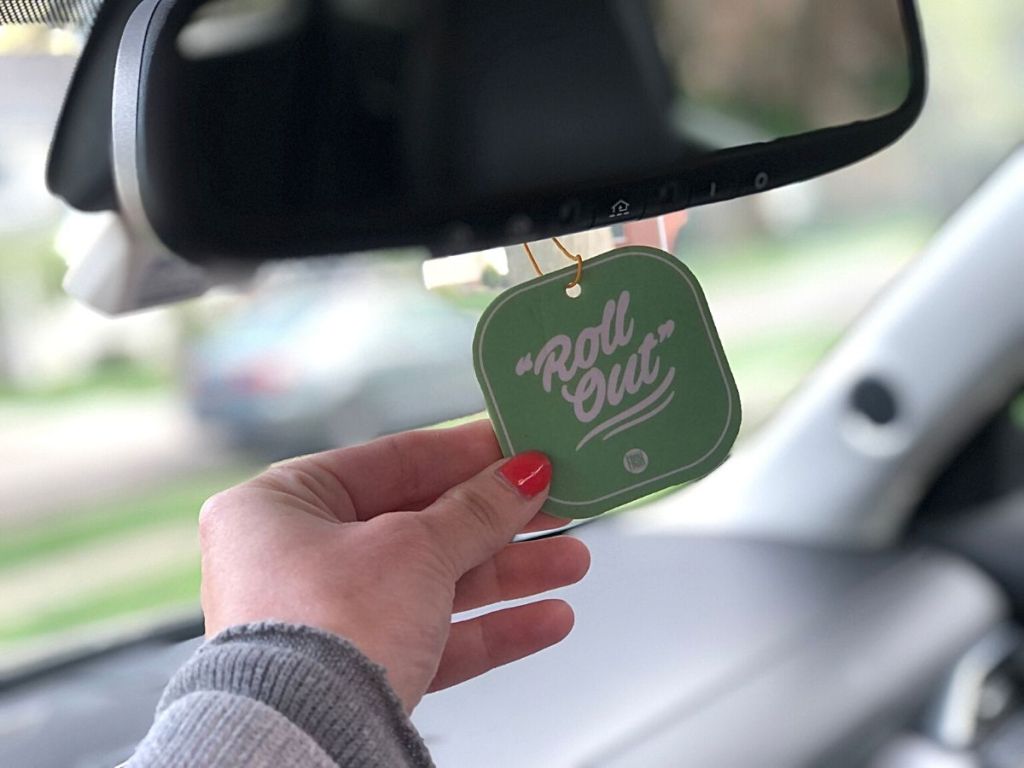 hand touching car air freshener hanging from review mirror that reads "Roll out"