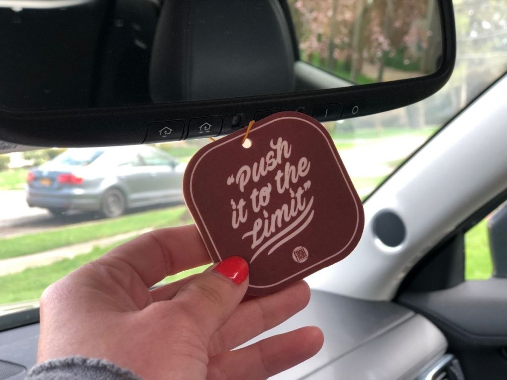 hand touching car air freshener hanging from review mirror that reads "Push it to the limit"