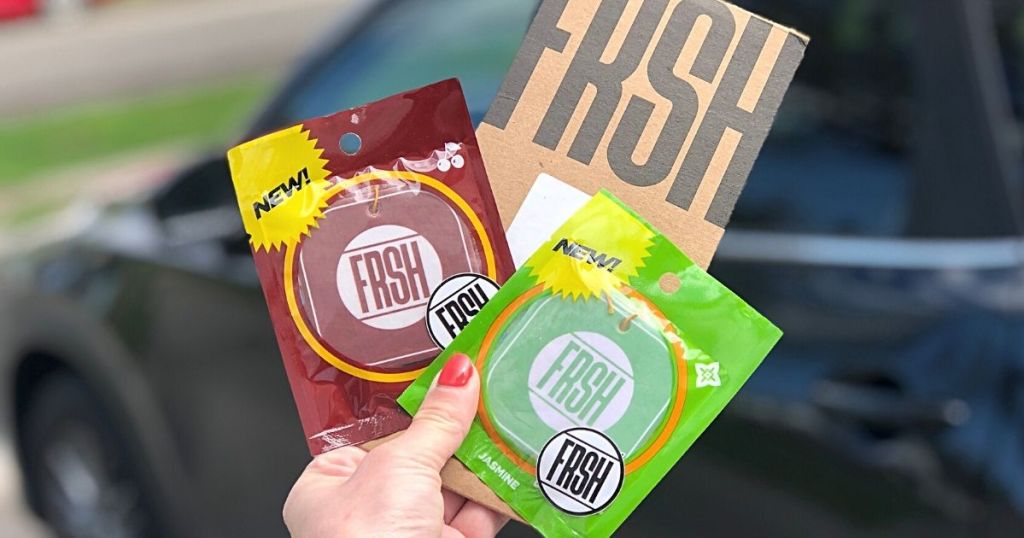 hand holding 2 FRSH car air fresheners with car in background