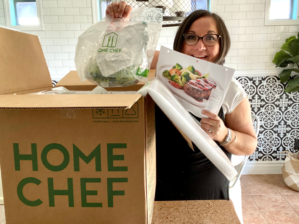 woman standing behind a home chef box holding recipe ingredients