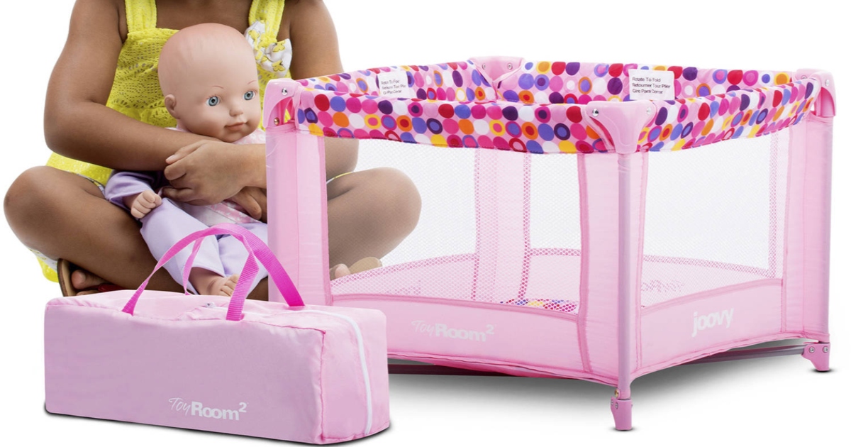 pink doll playard with child sitting beside it and a doll in her lap