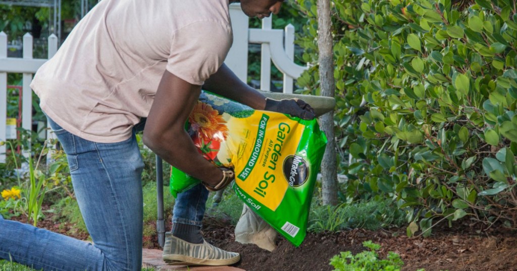 man kneeling out with a bag of miracle gro soil