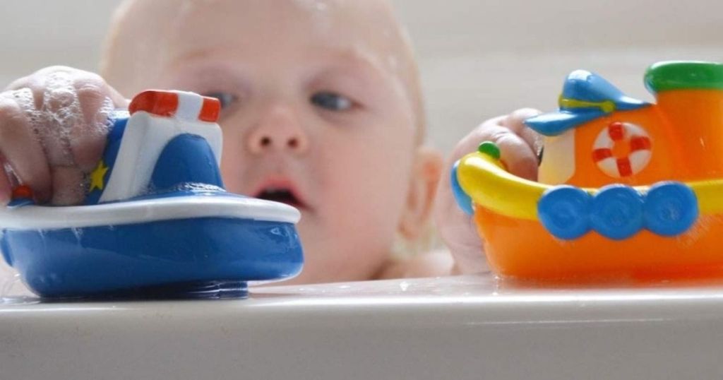 baby playing with Nuby Bath Toys on side of tub