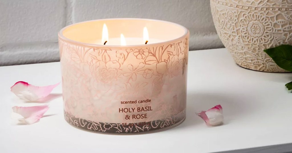 lit 3 wick candle on a white table with flower petals near it