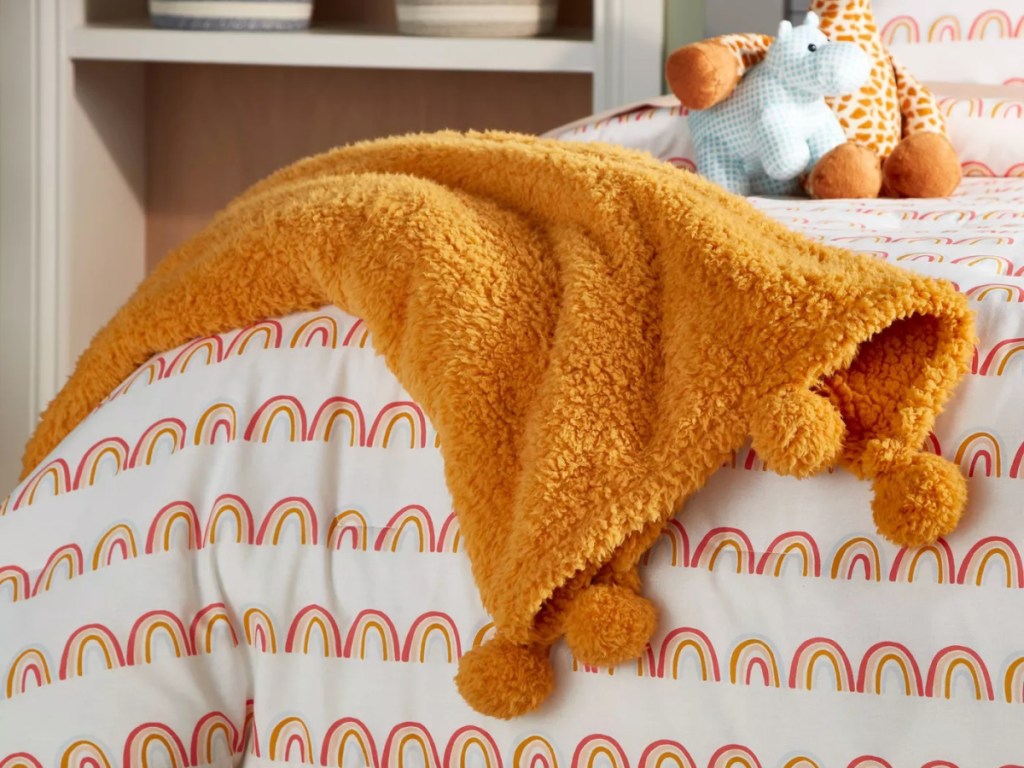 Pillowfort yellow pompom blanket across a child's bed