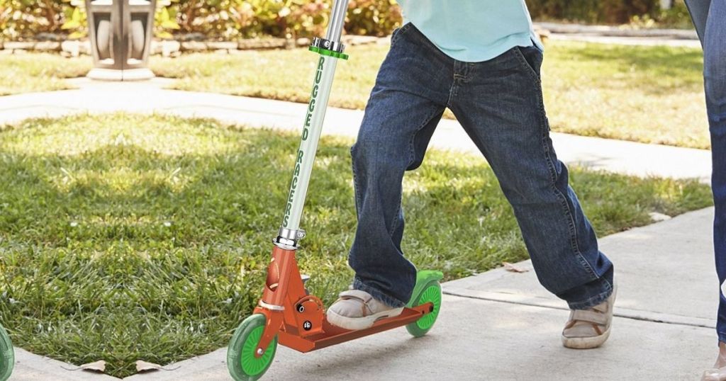 Little boy riding kick style scooter on sidewalk