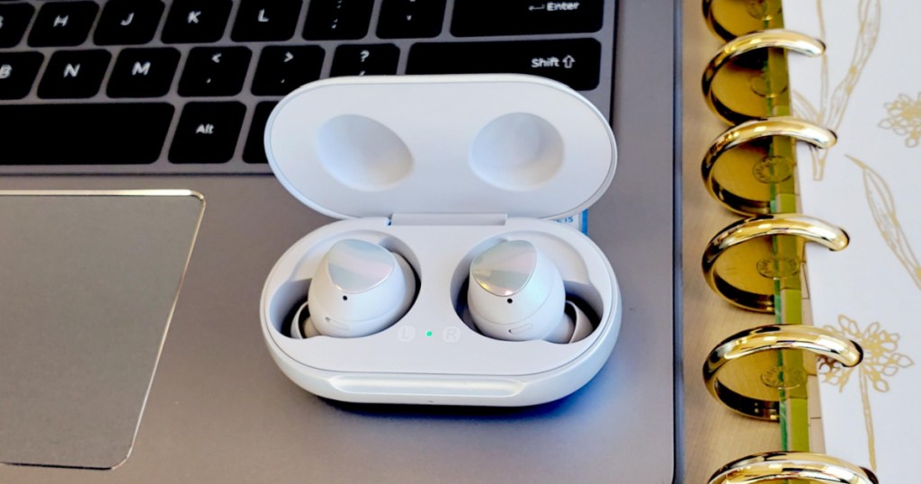 white earbuds in charging case sitting on laptop next to notebook