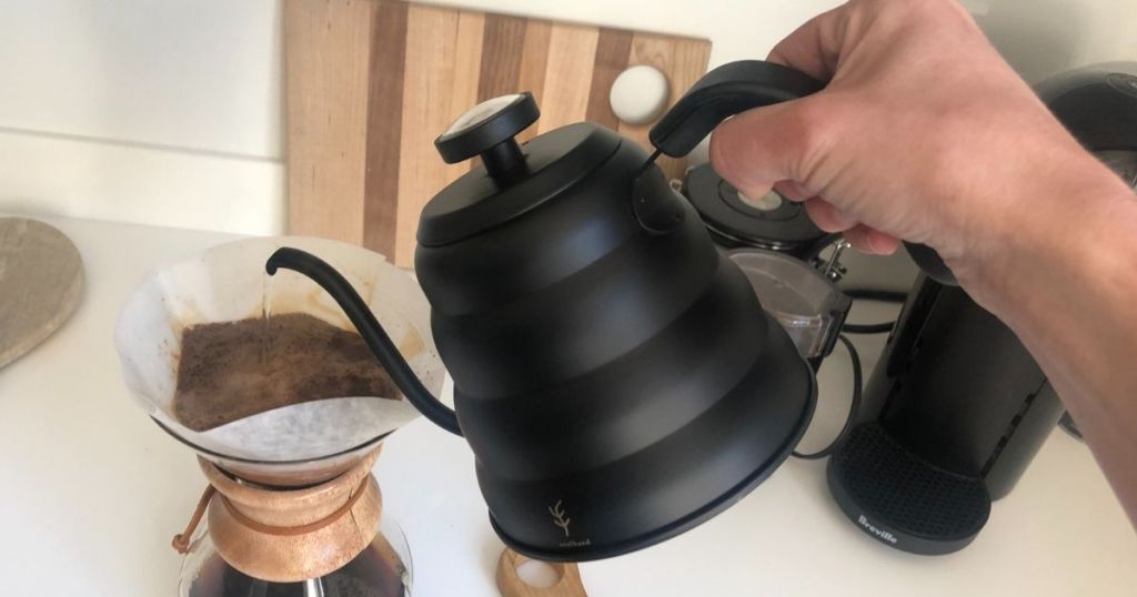 hand holding a kettle and pouring it over a coffee maker