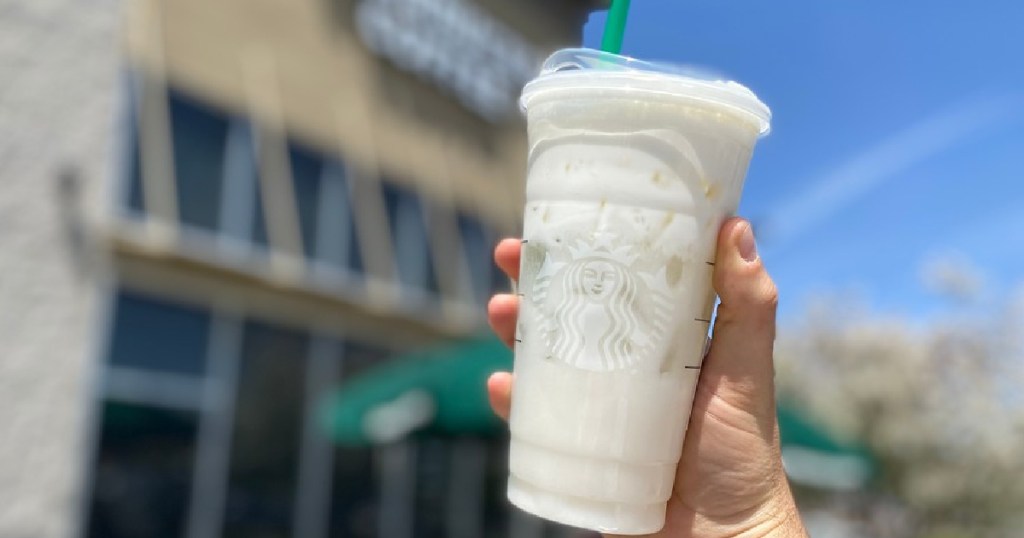 man's hand holding Starbucks iced drink outside in front of store