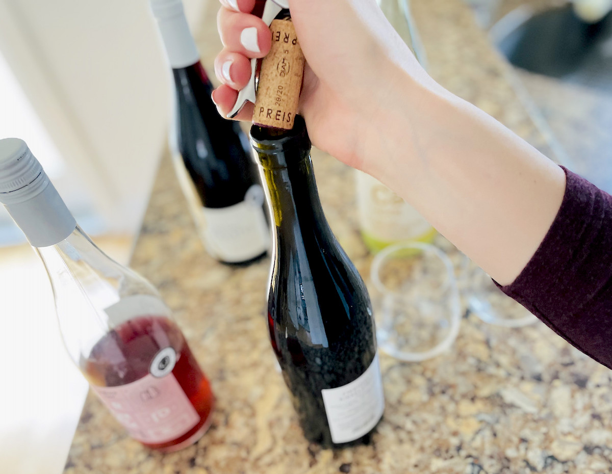 hand holding cork and wine bottle opener over bottle of dry farm wine