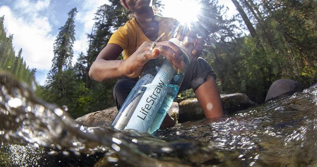 woman filling up Lifestraw water bottle from river