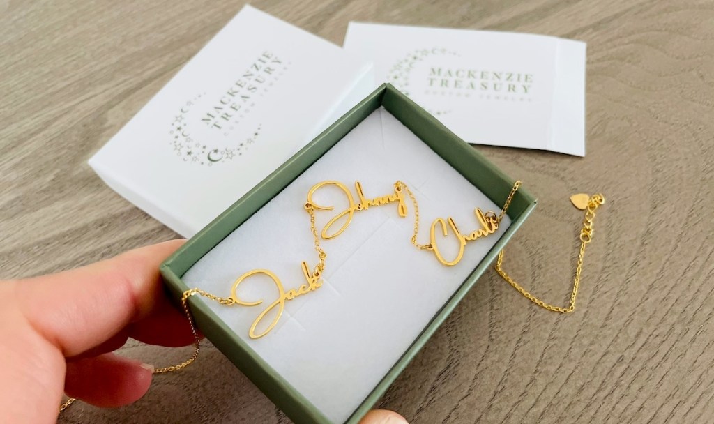 hand holding jewelry box with gold name necklace inside