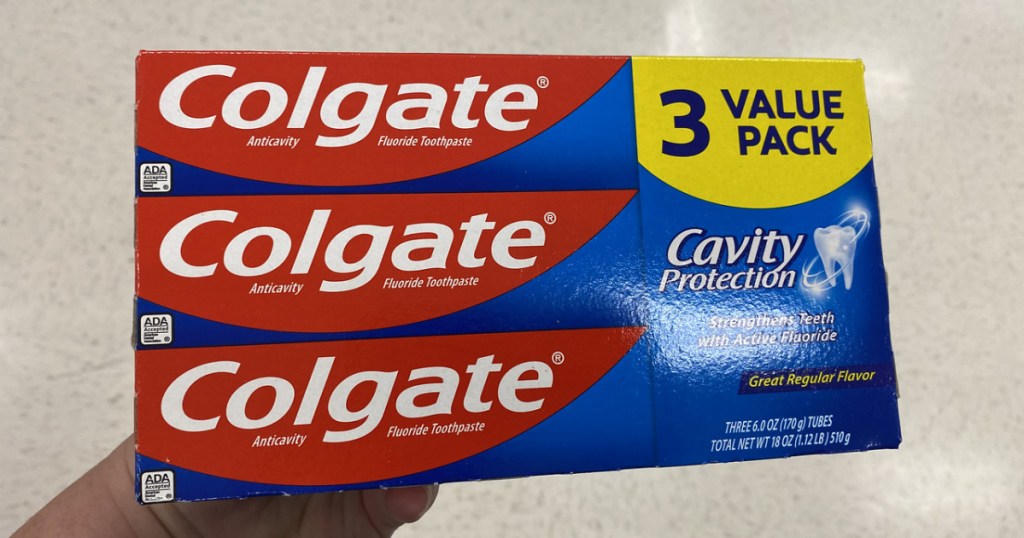 Hand holding up Colgate Toothpaste 3 pack