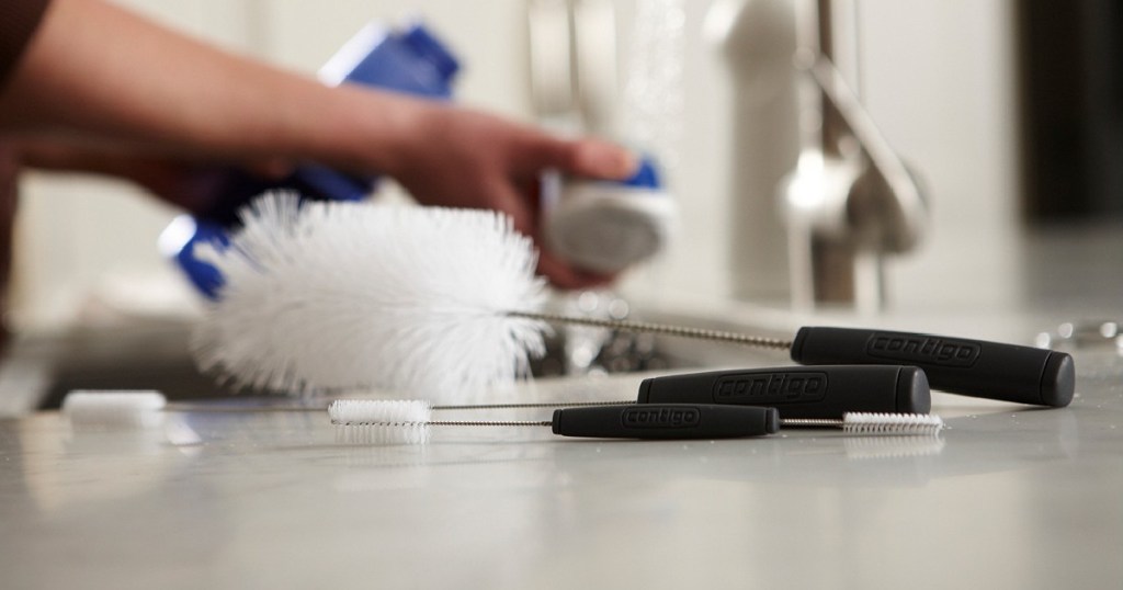 woman washing dishes and three bottle cleaning brushes on counter