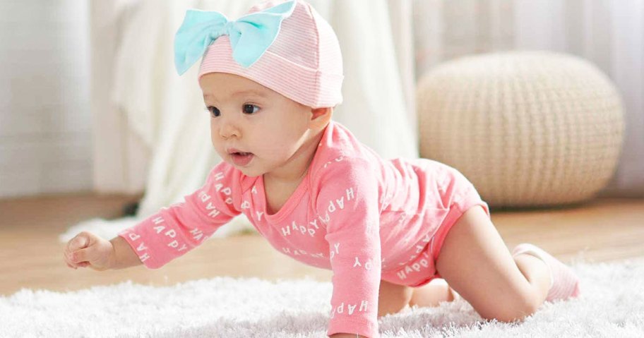 baby girl crawling on floor wearing pink onesie and hat with bow