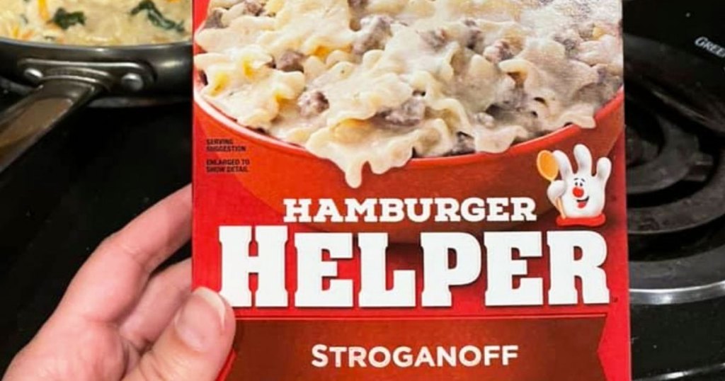 person holding box of hamburger helper in front of stove