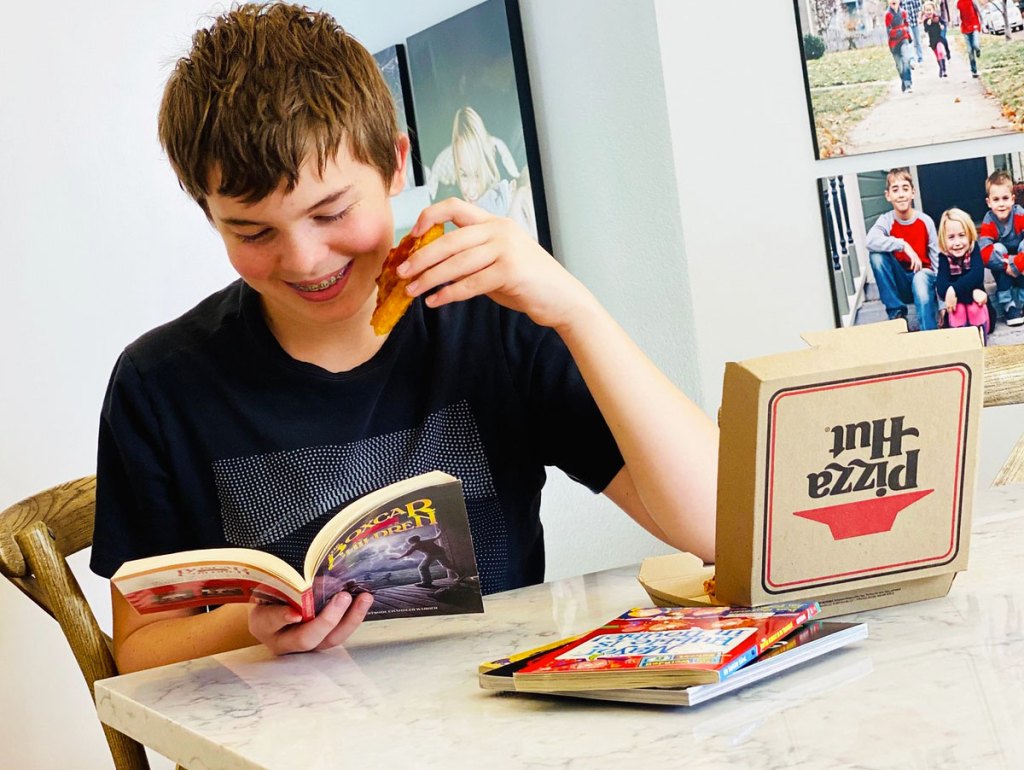 boy reading book and eating pizza hut