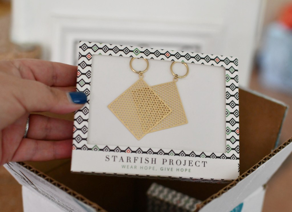 hand holding gold square starfish project earrings