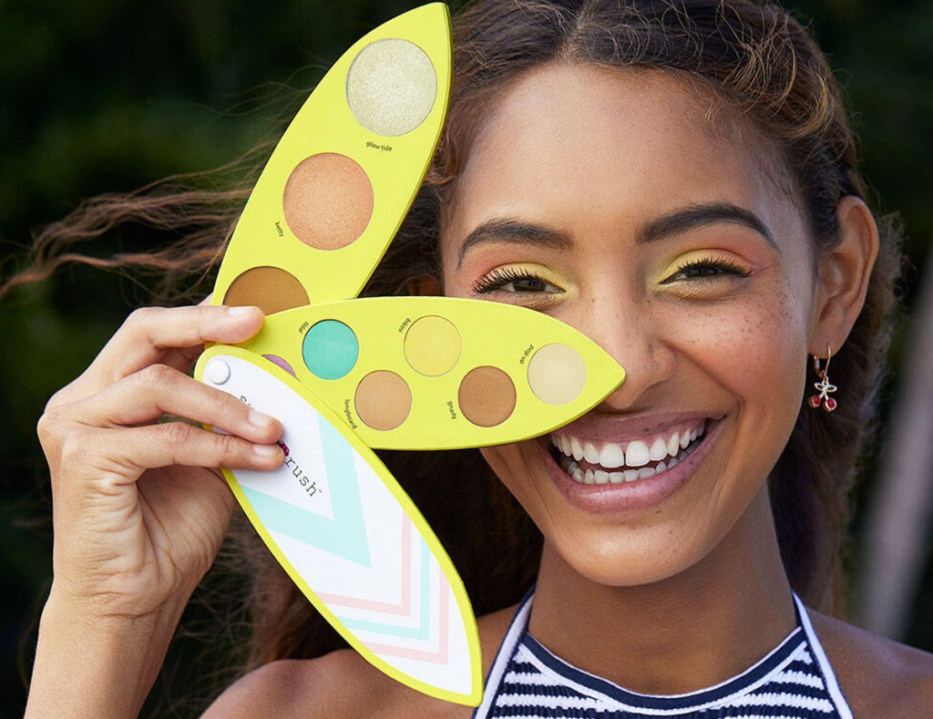 woman holding a surf board shaped eyeshadow palette next to face