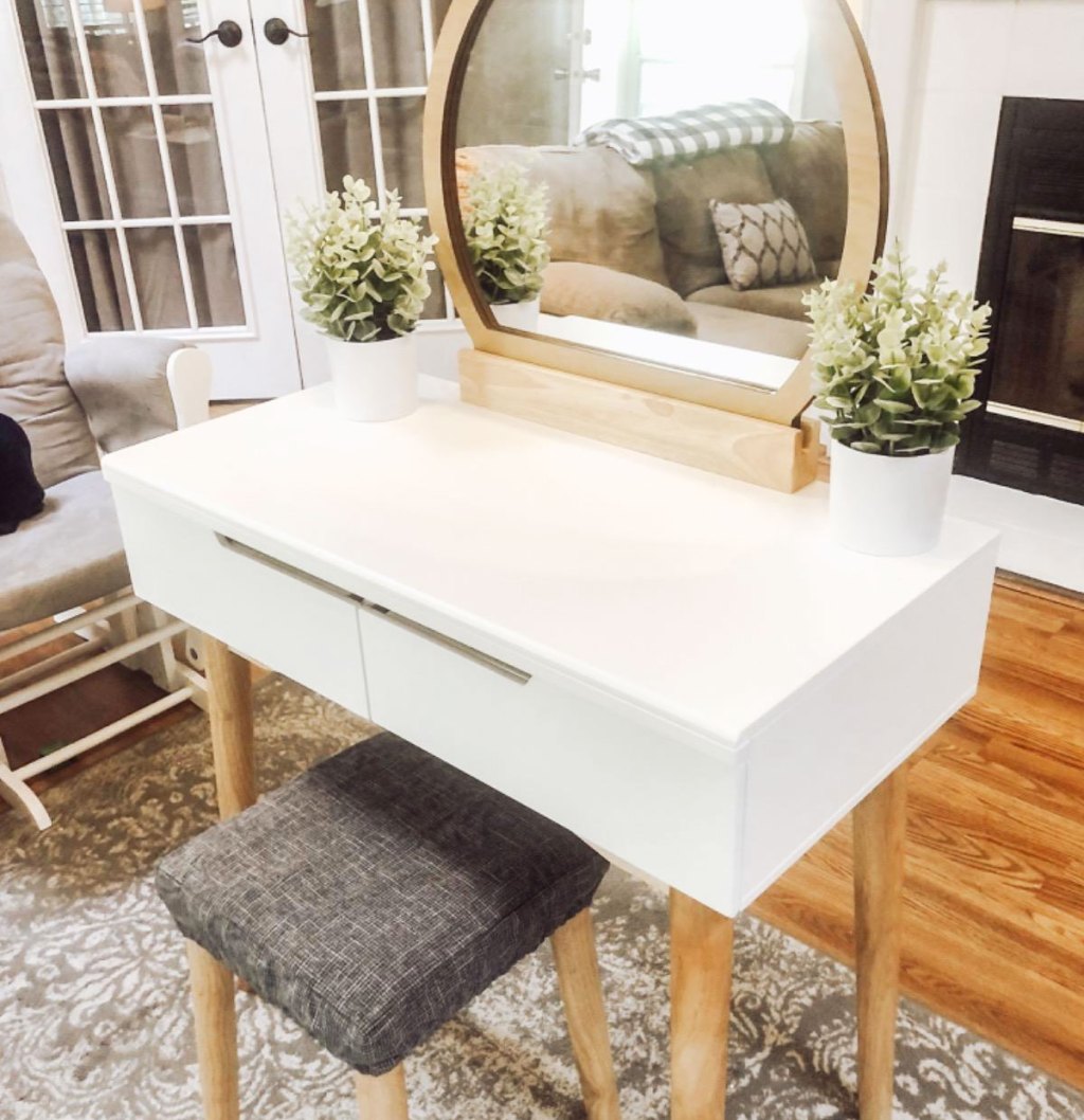 white makeup vanity with round wood mirror and grey stool