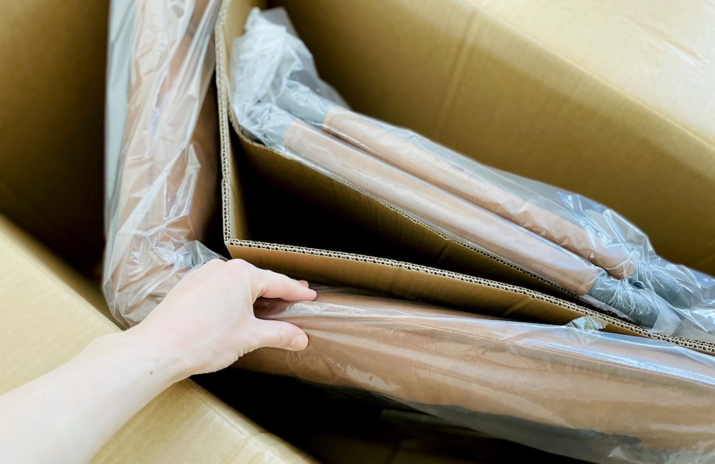 hand holding inside of box with plastic wrapped furniture