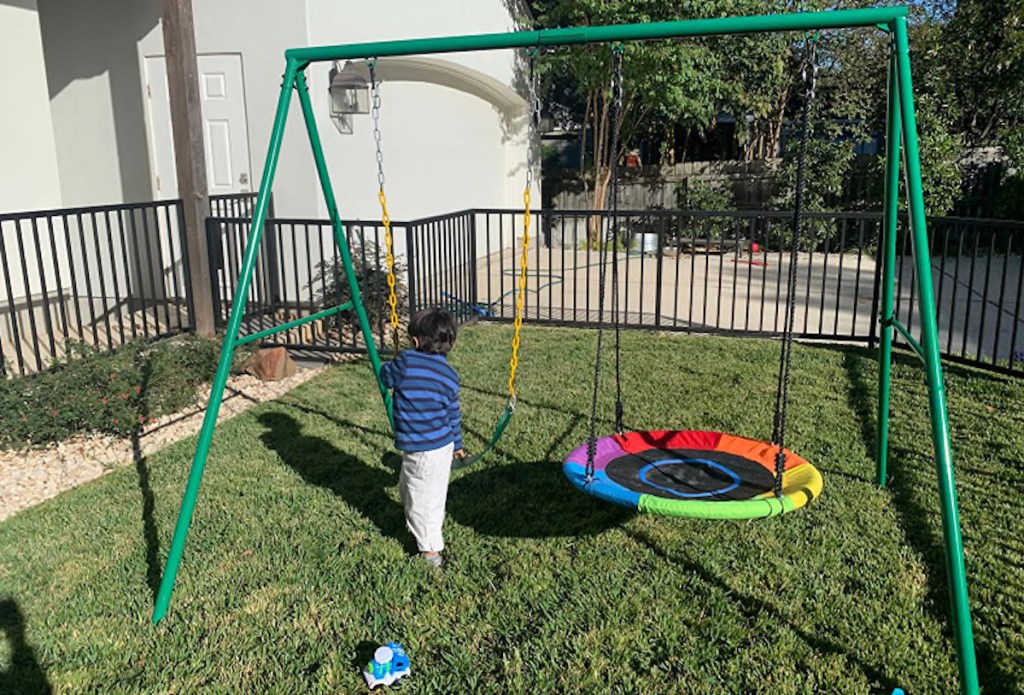 toddler boy playing on swing set outside in grassy yard