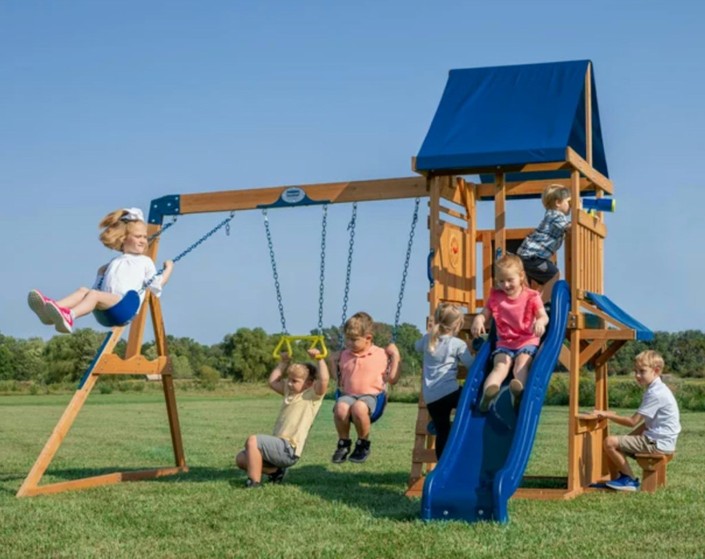 wooden swing set on sale with blue roof and slide and kids playing outside