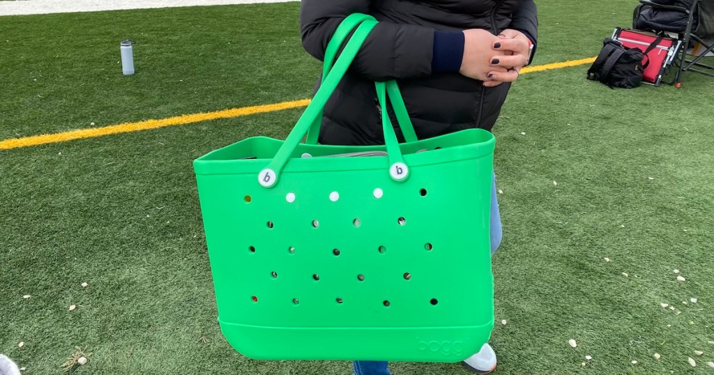 person holding bright green bogg bag on football field