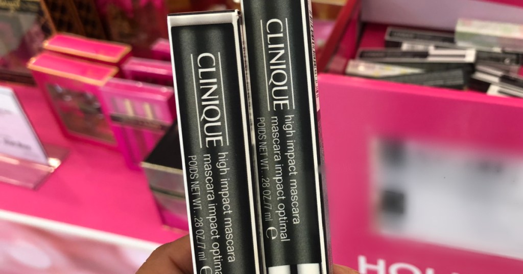hand holding 2 unopened packs of mascara by store display