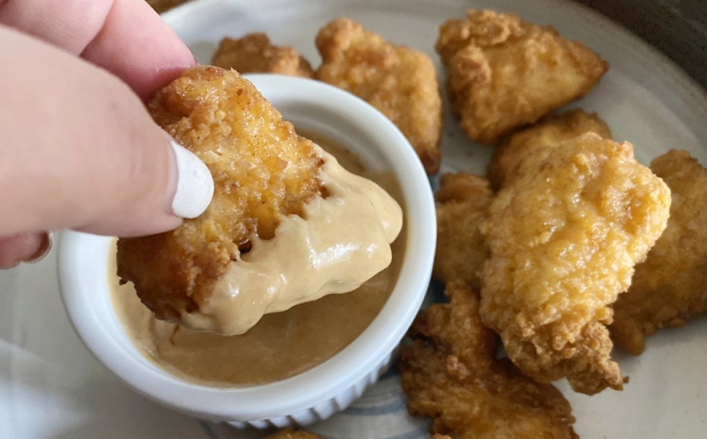 hand holding chicken nugget dipping into sauce