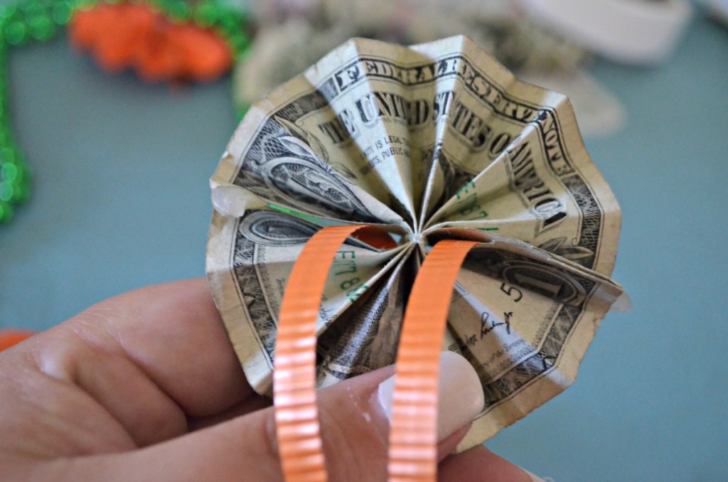 holding a rosette made from a folded dollar bill