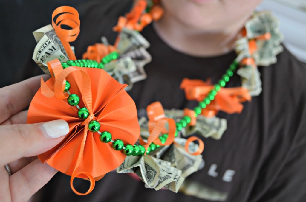 wearing a graduation lei made of orange paper and dollar bills