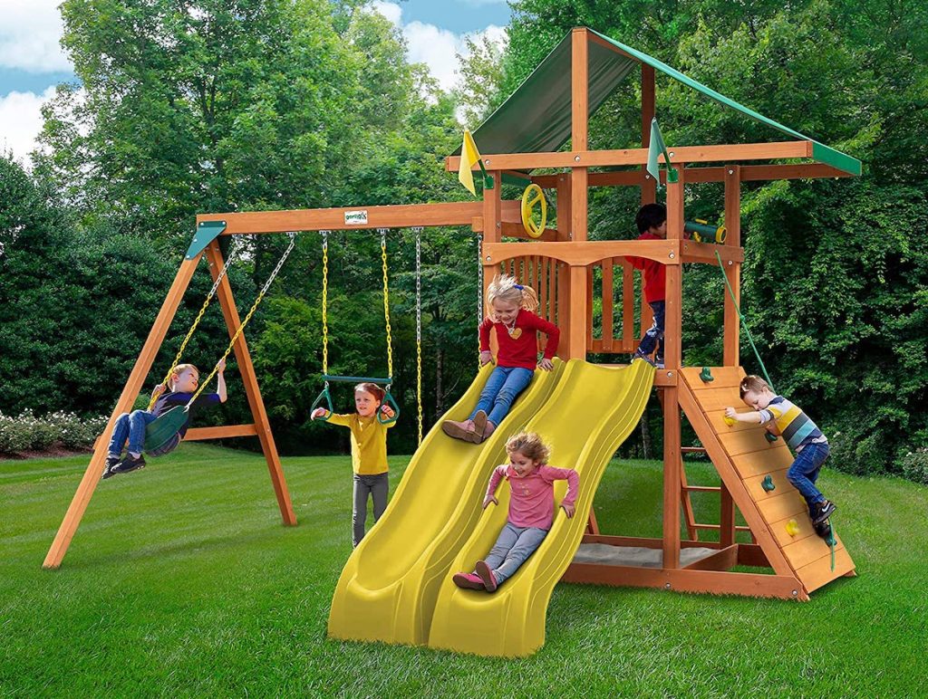 kids playing outside on wooden swing set with two yellow slides