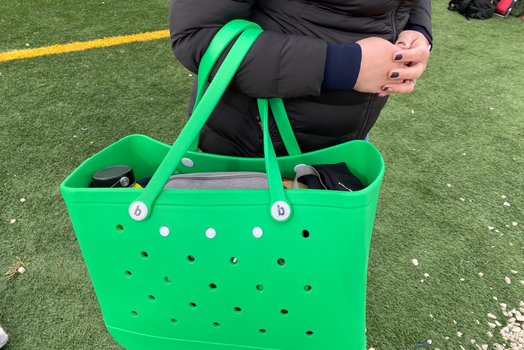 person holding bright green bogg bag on football field 