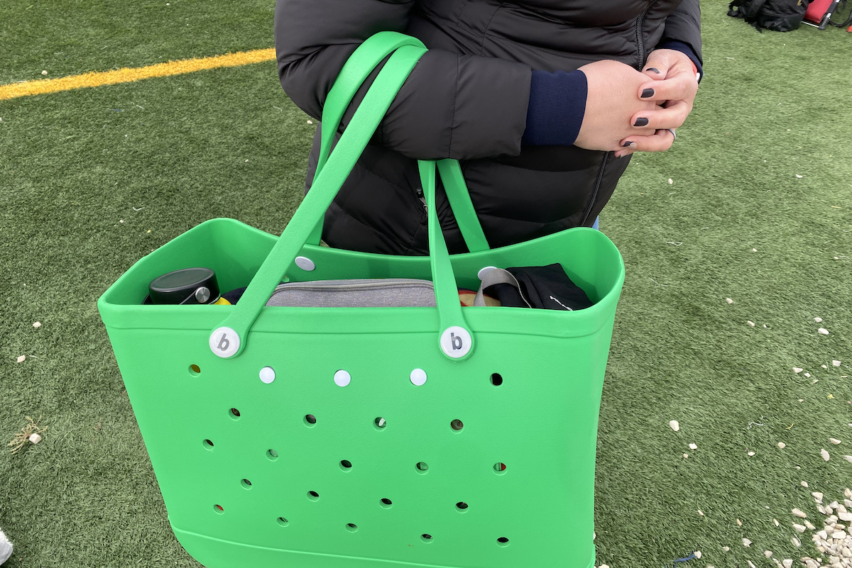 person holding bright green rubber beach bag on football field 