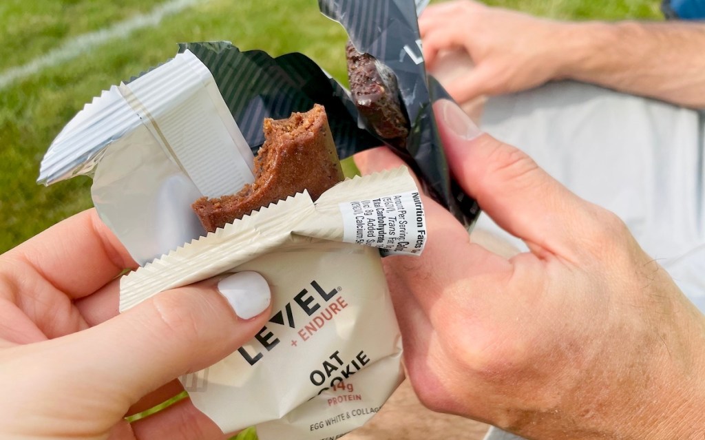 two hands holding different flavors of level foods protein bars