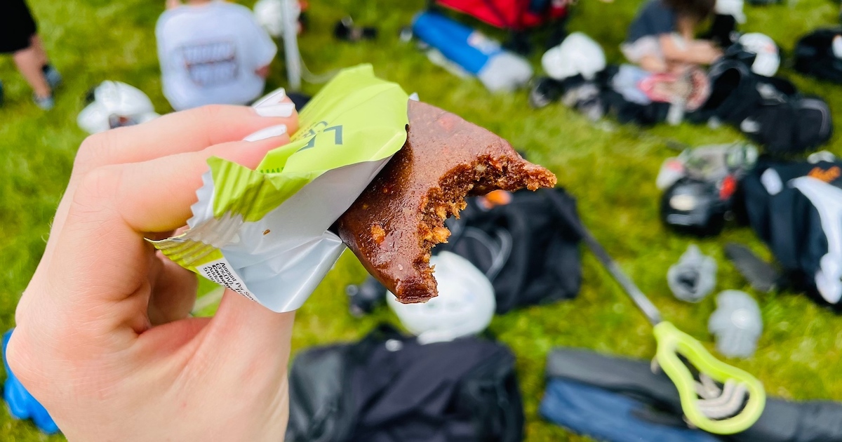 hand holding unwrapped protein bar with sports equipment in background