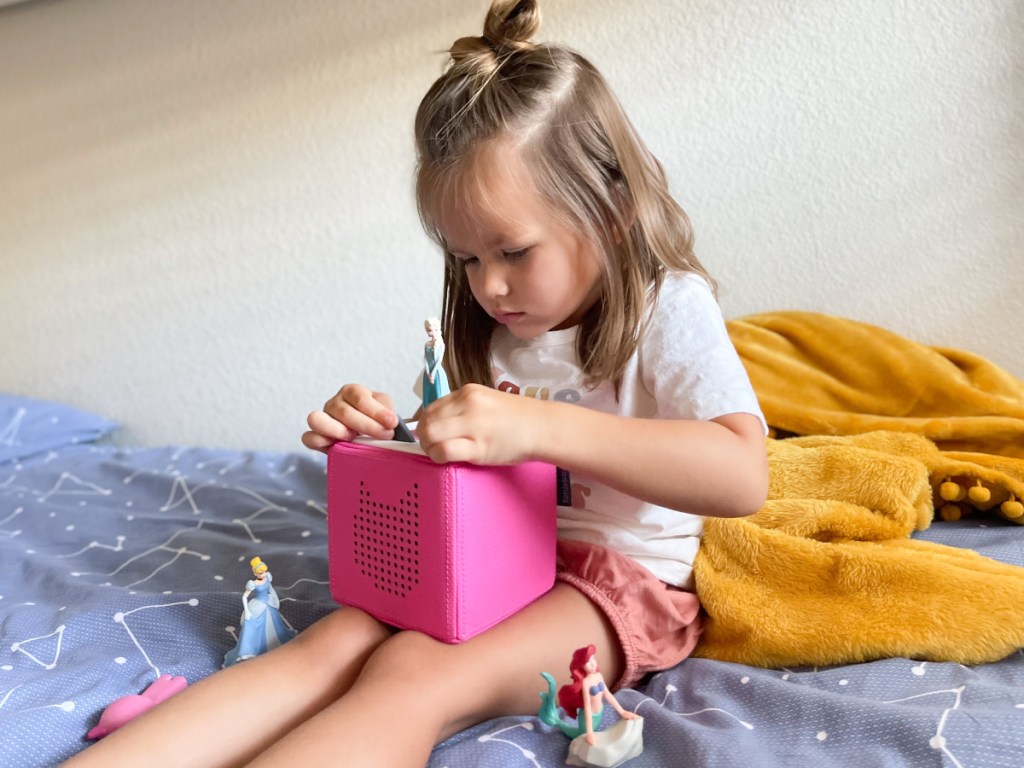 little girl using toniebox on bed 
