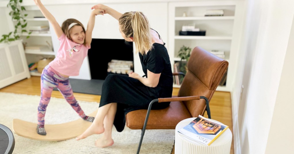 girl playing on balance board next to woman on leather sling chair