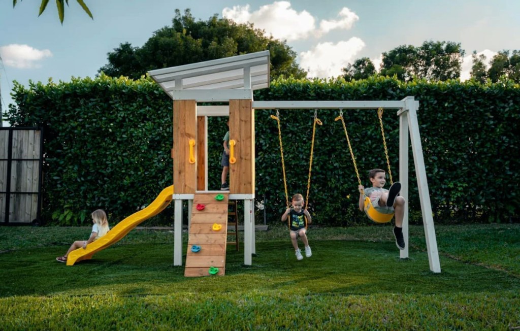 modern swing set with yellow slide outside in grass