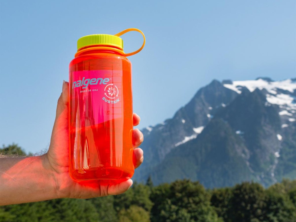 hand holding red water bottle in front of mountain range