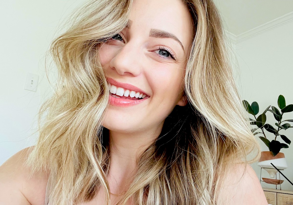 woman smiling with curled hair in her face and showing off the effects of her teeth whitening products